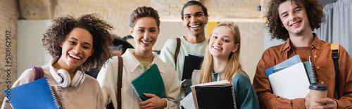 young and cheerful multiethnic students with copybooks smiling at camera, banner.