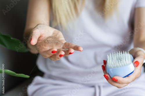 Portrait of stressed young blonde balding woman looking at unhealthy hair on brush, checking dandruff, upset by hair loss problem, alopecia at home. postpartum period, menstrual or endocrine disorder