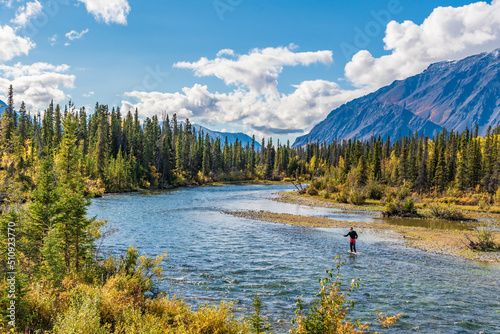 One person fishing in northern Canada during fall with scenic mountains in the background. 