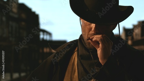 Portrait of cowboy smoking a cigar, old wild west city in the background. Spaghetti, macaroni western style cinematic footage