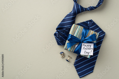 Father's Day concept. Top view photo of stylish giftbox with silk ribbon bow and postcard blue necktie and cufflinks on isolated pastel grey background