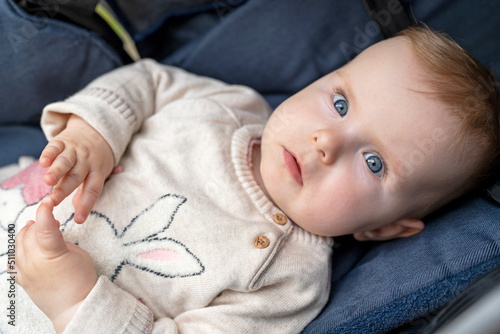 Beautiful baby with blue eyes and blonde hair looks at the camera. Adorable baby of 10 months in a knitted sweater lies in a stroller.