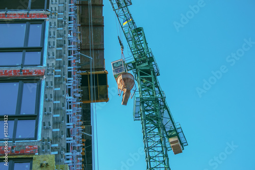 A crane lifts concrete for a modern metal-concrete structure of a residential building. Container with concrete against the blue sky.