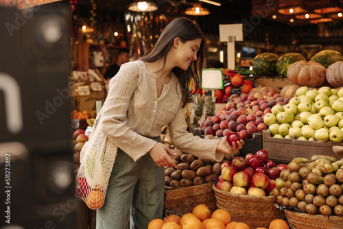 Pretty young caucasian brunette woman at fair chooses fresh ripe fruits. Girl is looking for good option for her diet. Healthy food concepts