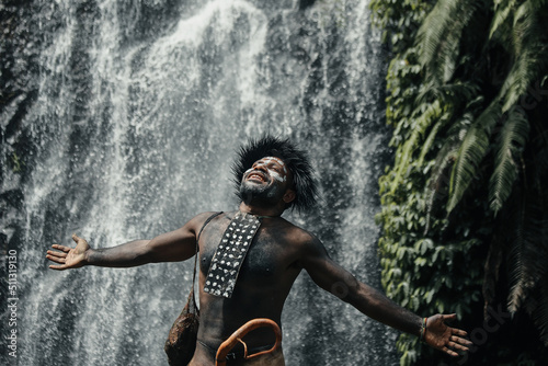 Papua man of Dani tribe feel free spread out his hands and breath against waterfall at greenery forest