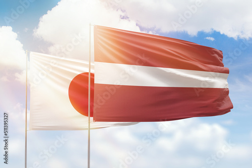 Sunny blue sky and flags of latvia and japan