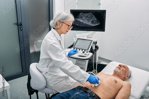 Ultrasound specialist doing ultrasonography of abdominal cavity for mature male patient with ultrasound machine at hospital
