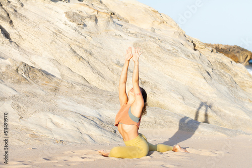Inspired woman in her yoga meditating style in the sand of a lonely beach on sunset with stone background - Praia do Gincho - Portugal 