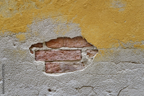 Mur jaune ancien avec enduit manquant et briques apparentes.