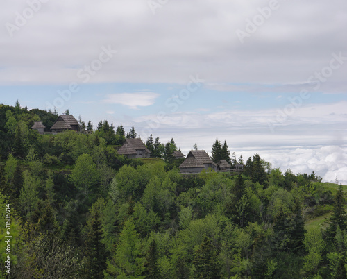 Traditional Shepard cottages on the top of the forested hill with the cloudy sky in the background, Velika Planina, Slovenia