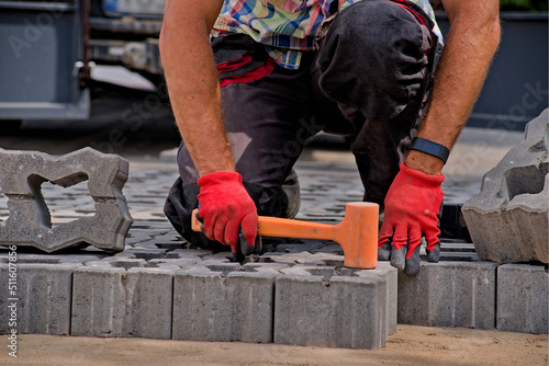 Majster ( foreman ) brukarz układa betonową kostkę brukową . Brukowanie podjazdu ażurowymi bloczkami betonowymi z malutkimi dziurkami . Mistrzowsko wybrukowany podjazd . W użyciu pomarańczowy młotek.
