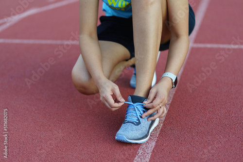 Choseup of Asian young woman tying shoes laces on athetic track in outdoor gym.
