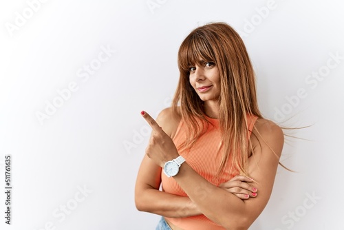 Hispanic woman with bang hairstyle standing over isolated background pointing with hand finger to the side showing advertisement, serious and calm face