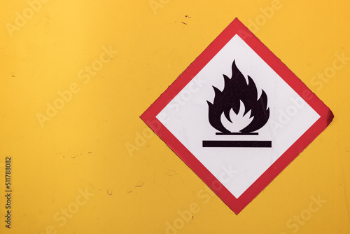 Traditional white, red and black flammable fire icon diamond sticker against a bright yellow wall.