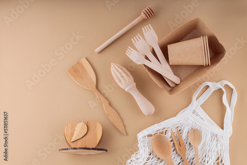 Eco-friendly kitchen utensils, paper disposable tableware and mesh bag. Wooden cutlery and shopping bag on a beige background. Sustainable lifestyle. Zero waste concept