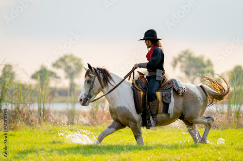 One cowboy with hat control horse to walk through grass field cover by water near river and show some splash during walking.