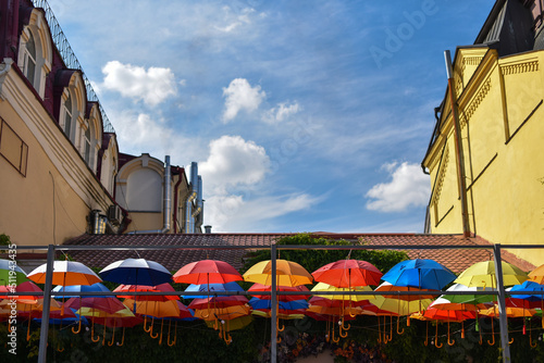 multicolored umbrellas hanging over restaurant terrace on background old architecture and blue sky