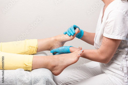 A pedicurist massages the client's feet. Close-up of legs and toenails with titanium thread and master's arms. The concept of chiropody and podology