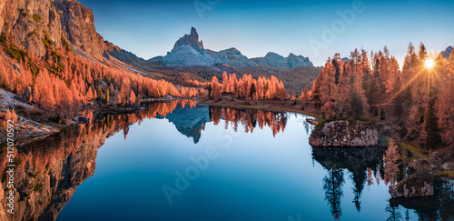 Panoramic autumn view from flying drone of popular tourist destination - Federa lake among red larch trees. Impressive sunrise in Dolomite Alps. Gorgeous morning scene of Italy, Europe.