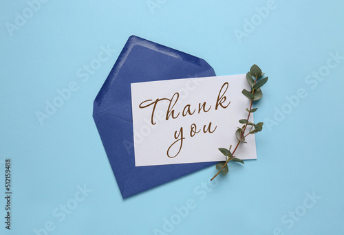 Card with phrase Thank You, envelope and branch of eucalyptus on light blue background, flat lay