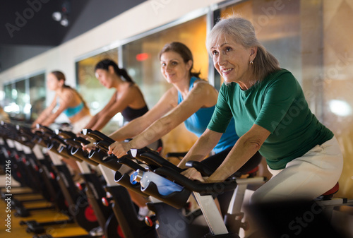 Portrait of confident adult woman training on fitness bike in gym indoor