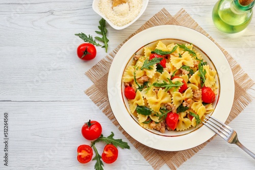 Italian Traditional Dish"Pasta con salsiccia e rucola",pasta with Italian sausage,arugula,cherry tomatoes,olive oil,white wine,salt and peppers on plate with white wood background.Top view