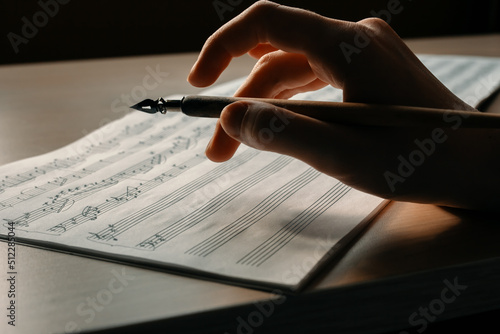 Woman's hand with a pen drawing notes in a music book, writing a melody by hand, composing music