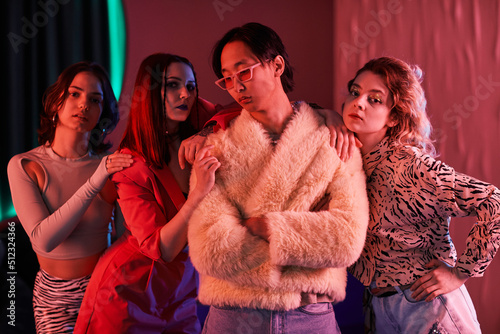 Group of young girls posing with extravagant Asian man in nightclub lit by pink neon light