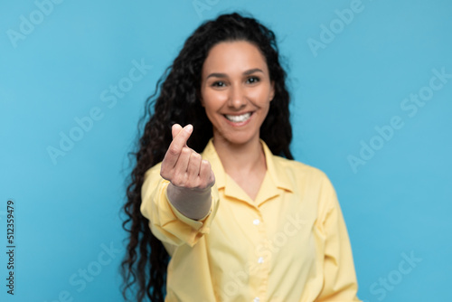 Beautiful young woman making Korean finger mini heart gesture on blue studio background, selective focus