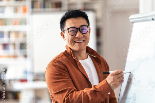 Positive Asian Teacher Man Smiling Writing On Whiteboard In Classroom