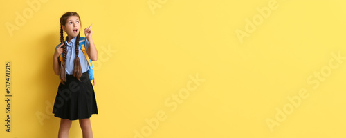 Cute schoolgirl pointing at something on yellow background with space for text