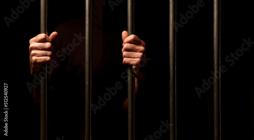 hands of a prisoner behind prison bars on black background