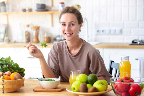 Healthy lifestyle, diet, weight loss concept Beautiful happy woman eats breakfast looking at the camera and smiling friendly Beautiful female eating fresh salad while sitting in kitchen Vegan meal