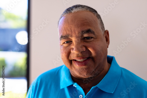 Close-up portrait of smiling biracial senior man against white wall in retirement home, copy space