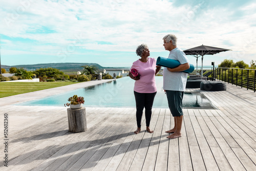 Multiracial senior friends with exercise mats standing on hardwood floor against sky at nursing home