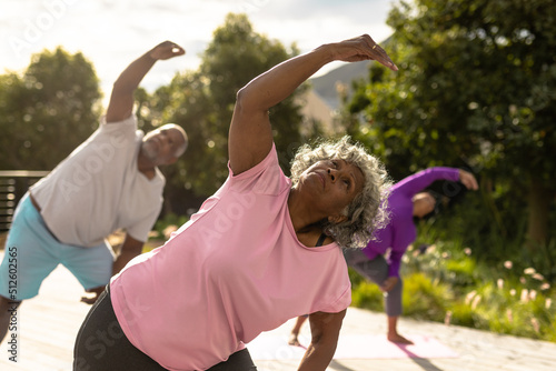 Multiracial senior friends practicing yoga against plants in yard during summer