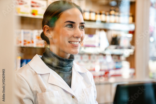 White apothecary wearing lab coat smiling while working in pharmacy