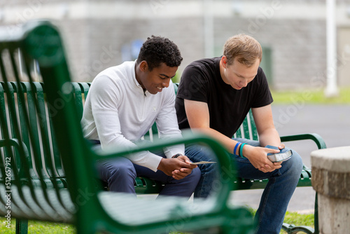 Two men sitting on a park bench praying together