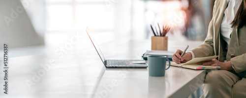 Businesswoman writing note, sitting at her desk in modern office.