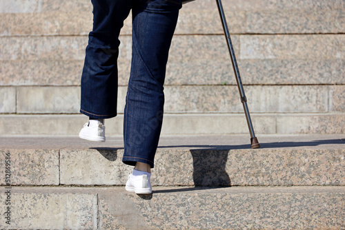 Woman wearing jeans with walking cane climbing stairs outdoor, legs in motion on the street steps. Concept for disability, limping adult, diseases of the spine, old people