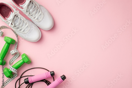 Sports accessories concept. Top view photo of white shoes tape measure green dumbbells and skipping rope on isolated pastel pink background with empty space