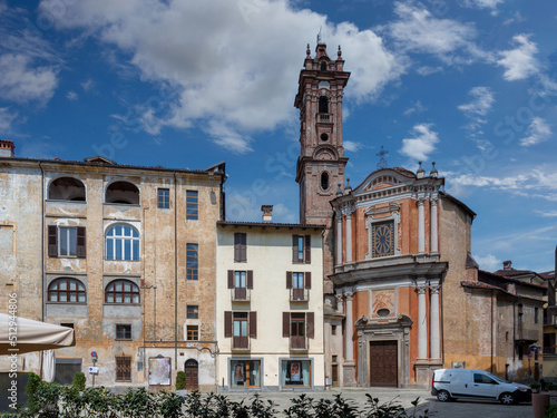 Savigliano, Cuneo, Piedmont, Italy - May 04, 2022: Church of the Confraternity of the Pietà with ancient buildings in Cesare Battisti square on blue sky with clouds