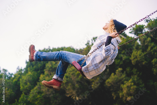 Joyful and youthful woman flying high on a swing at the childhood park. Concept pf people and no limit age to play and have fun. Female in outdoors leisure activity using swing and enjoy life