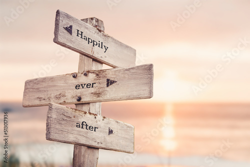 happily ever after text quote on wooden crossroad signpost outdoors on beach with pink pastel sunset colors. Romantic theme.