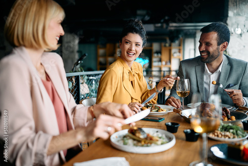 Happy entrepreneur talks to her coworkers during business lunch in restaurant.