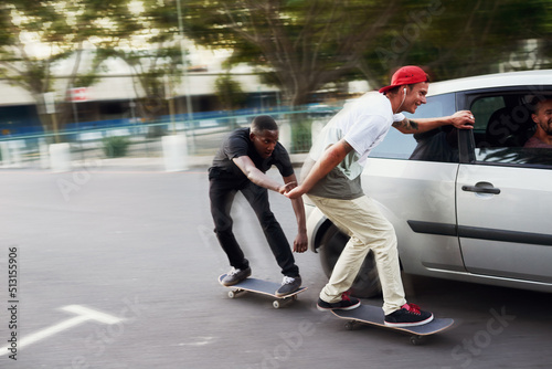 Never let your best friends do stupid things alone. Shot of two skaters holding on to a moving car.