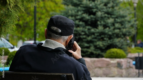 A man speaks on the phone on the street. The phone is attached to the ear. View from the back.