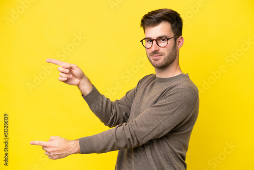 Young caucasian man isolated on yellow background pointing finger to the side and presenting a product