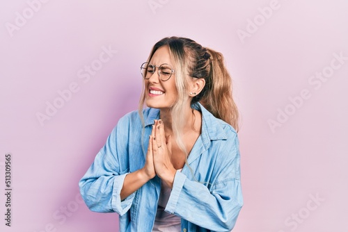 Beautiful young blonde woman wearing casual clothes and glasses begging and praying with hands together with hope expression on face very emotional and worried. begging.