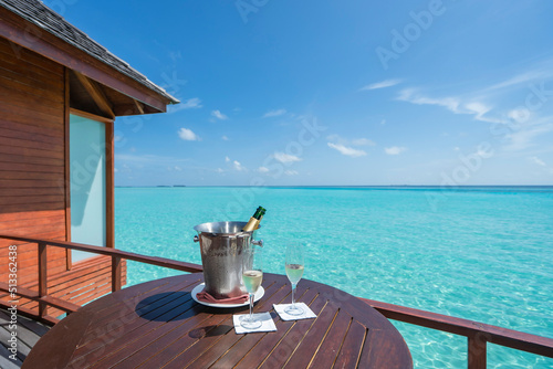  A bottle of champagne with ice bucket on table in over water sweet villa in Maldives island.